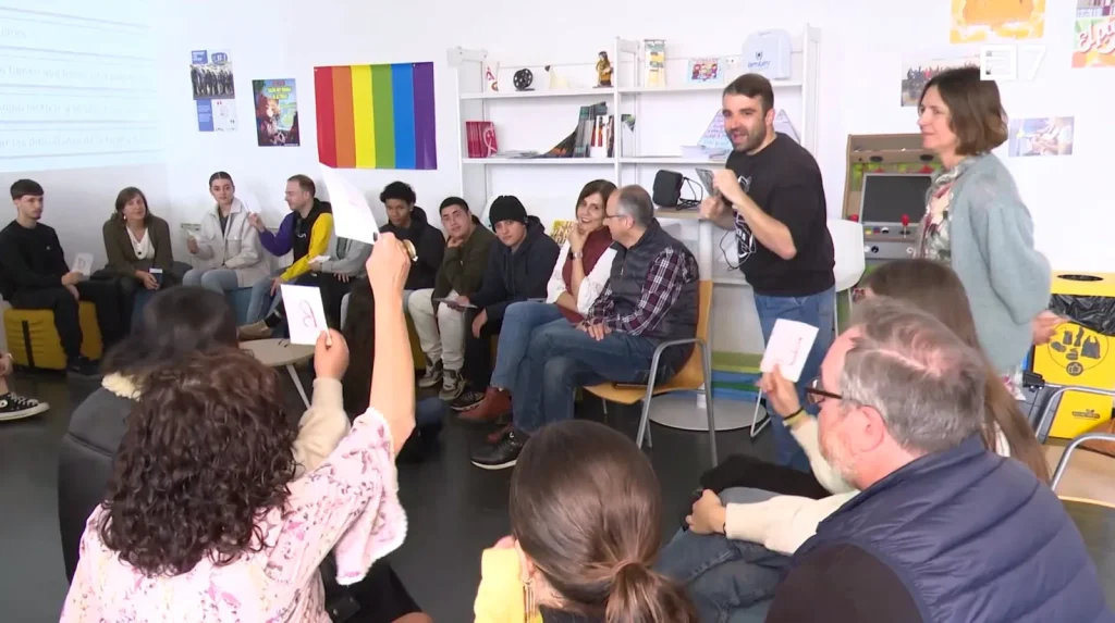 Participants in a circle during a TRANSIT workshop, with a facilitator speaking and a rainbow flag on the wall