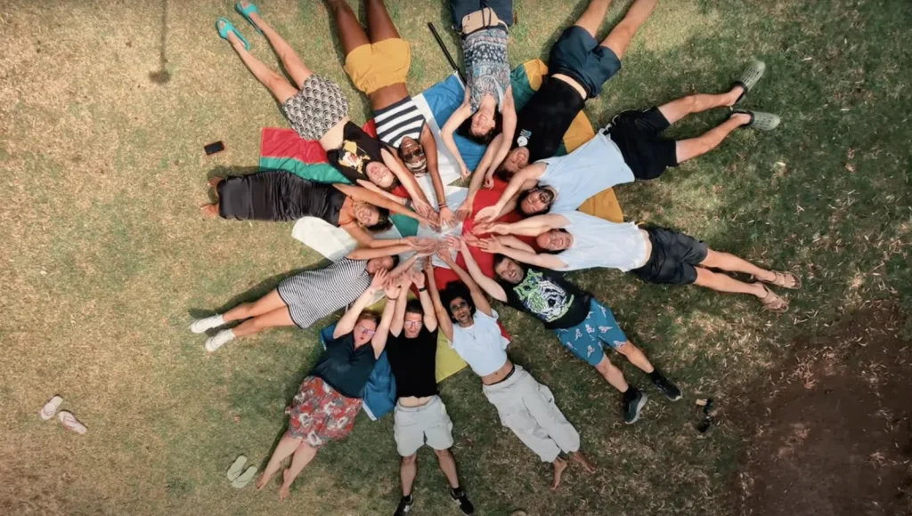 Overhead view of participants lying in a circle on grass, reaching their hands towards the centre